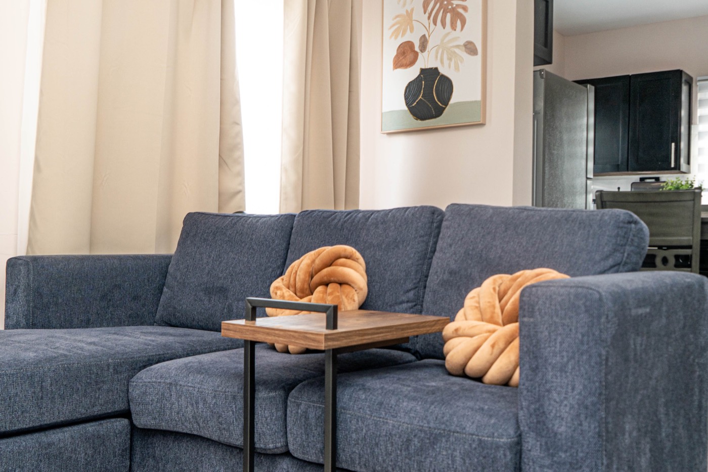 Sofa with knot cushions, artwork above, kitchen beyond